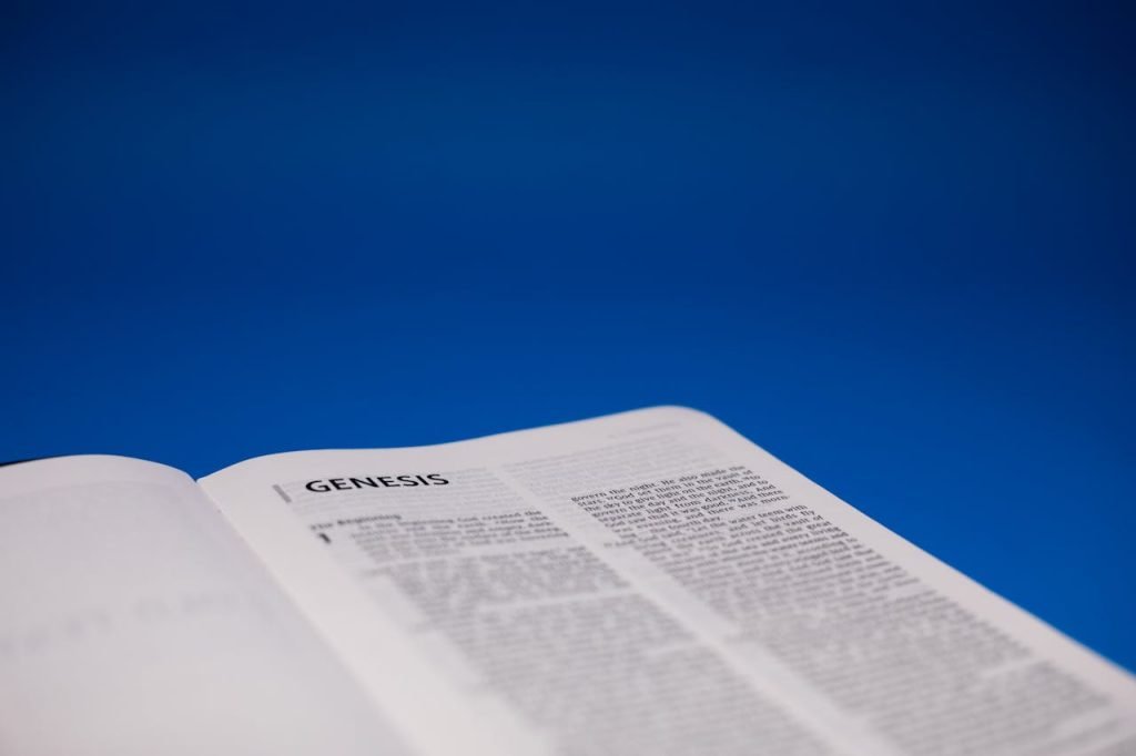 Close-up of an open Bible displaying Genesis against a vivid blue surface.