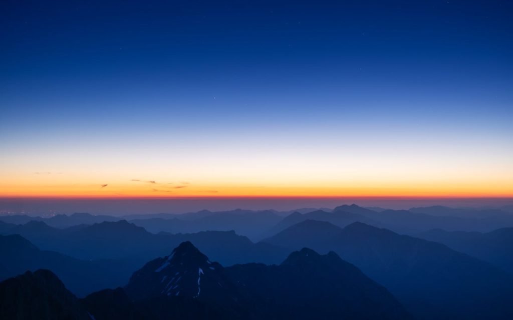A breathtaking view of the Alps at sunrise with vibrant orange and blue hues over mist-covered peaks.