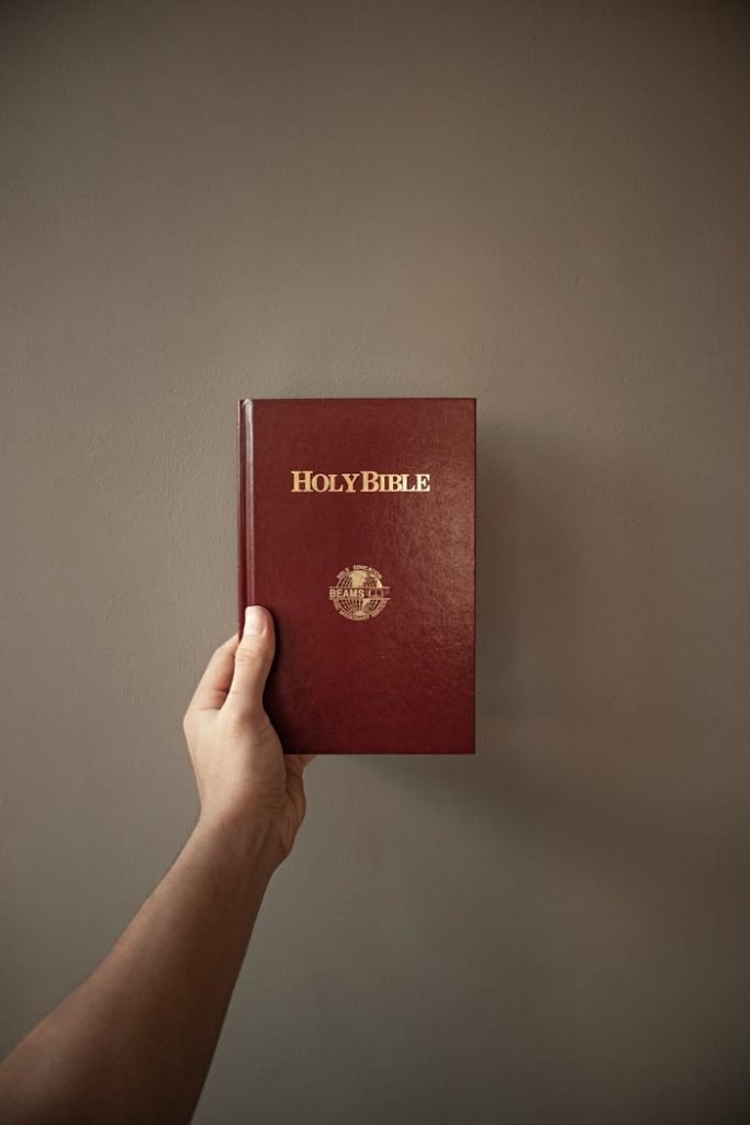 A person holding a red Holy Bible against a neutral wall background.